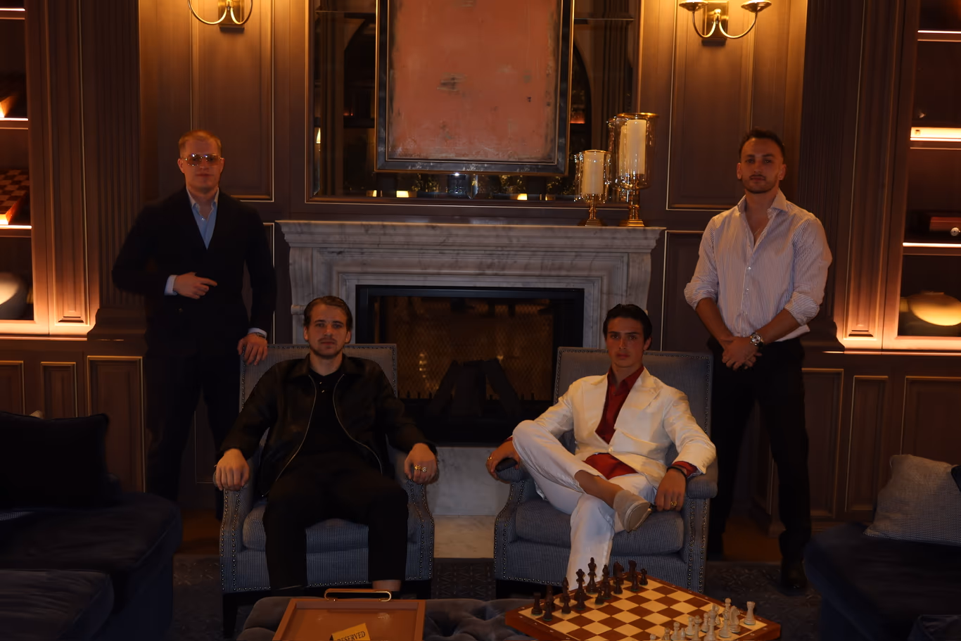 Four founders gathered around a fireplace lounge, a chess game mid-play on the table — a peer group that meets off the record