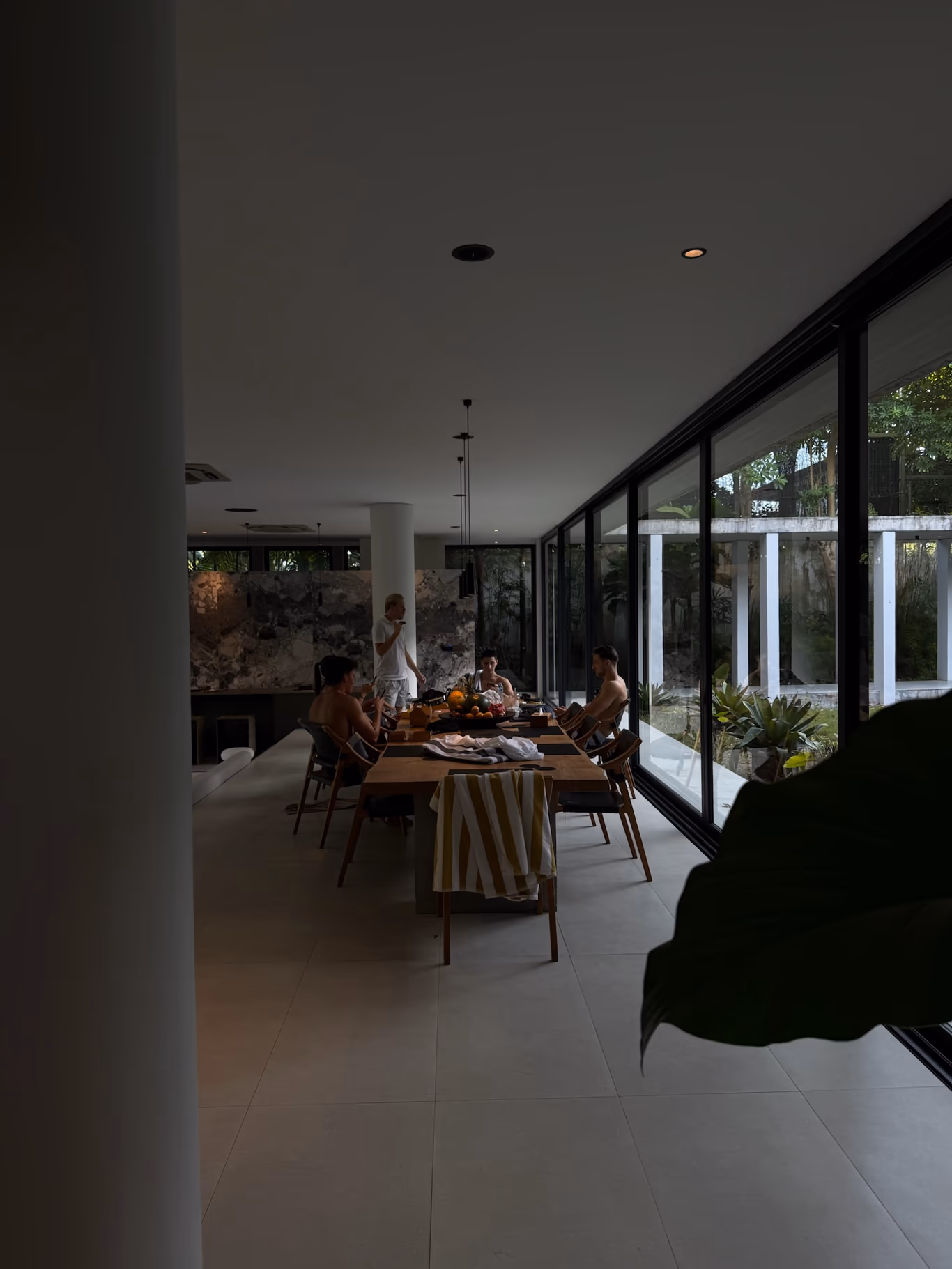 A small group around a long table in a glass-walled villa room — quiet company against founder loneliness
