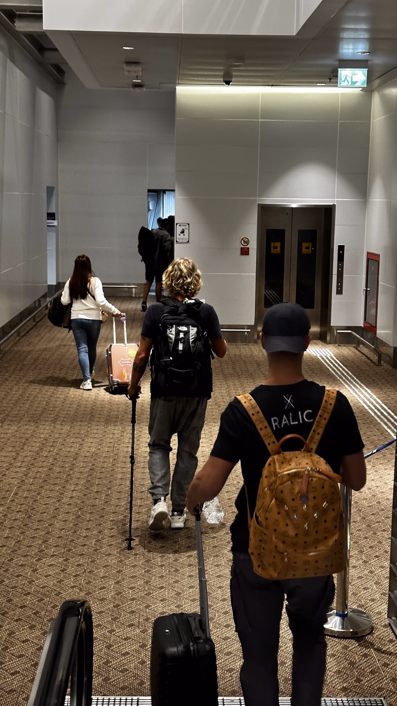 Founders wheeling rolling suitcases down a carpeted terminal corridor toward an elevator on a Helix trip